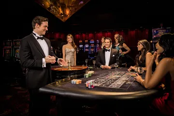 Um dealer profissional de smoking cumprimentando jogadores na mesa de roleta, simbolizando a autêntica sensação de cassino ao vivo no 1CCC.